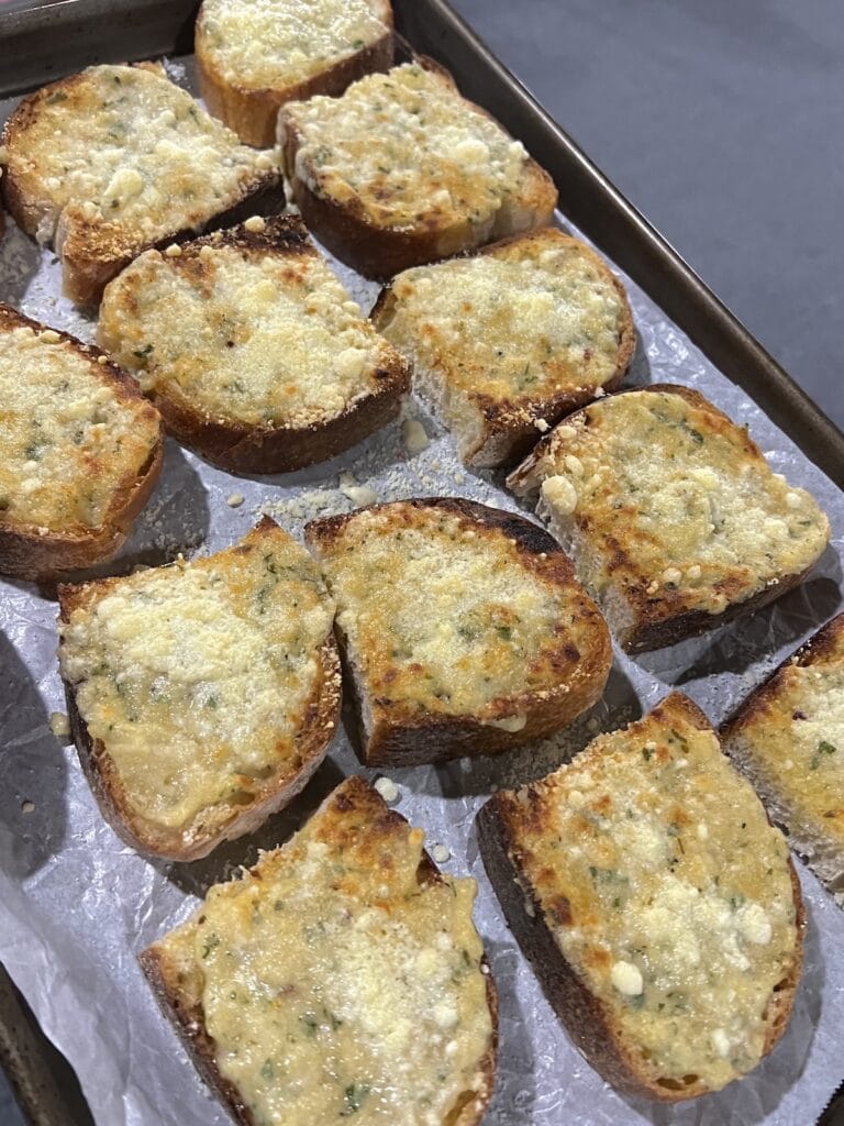 Several slices of garlic bread baguette on sheet pan after broiling.