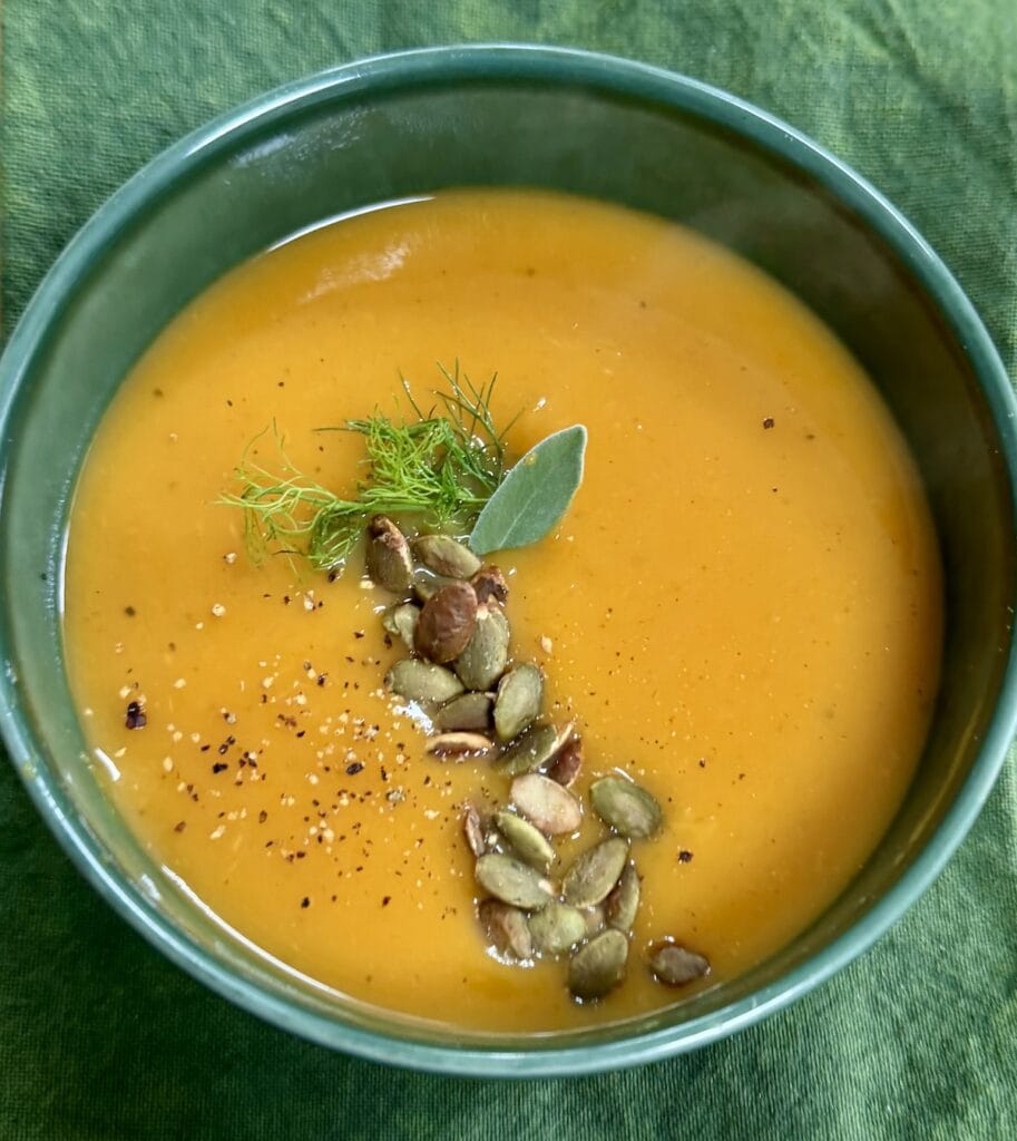 Roasted butternut soup with pumpkin seed garnish in green soup bowl over green towel.