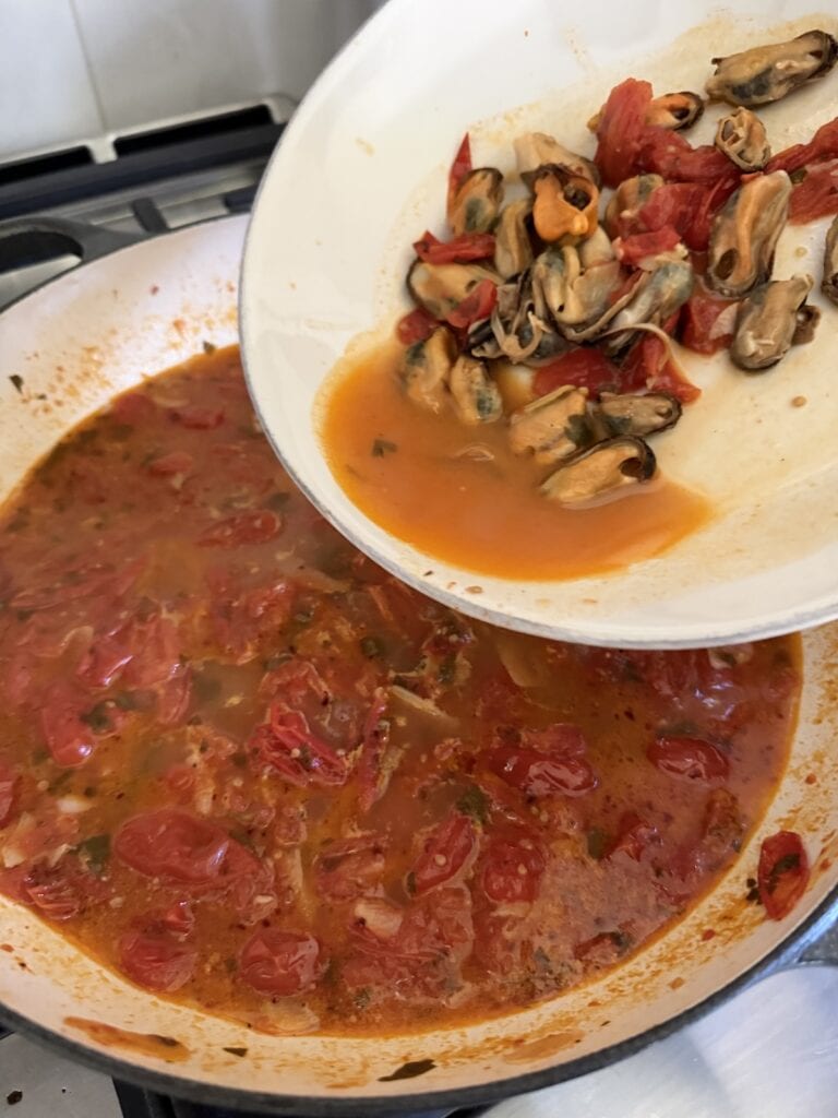 Adding shelled mussel meat back to sauce.
