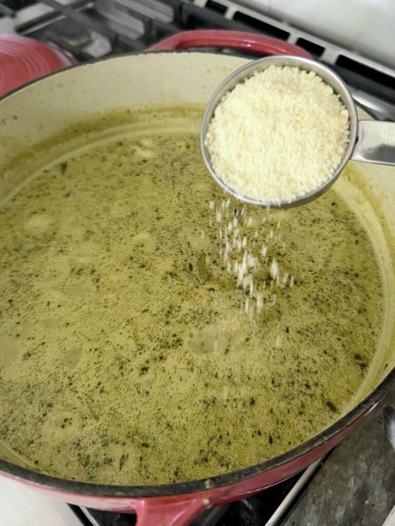 Adding grated cheese to potato gnocchi sausage soup.