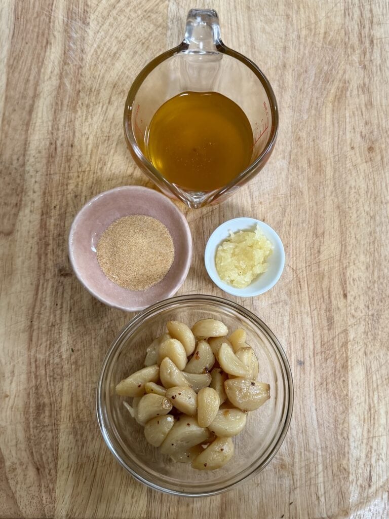 The four different forms of garlic in the garlic butter recipe on cutting board: garlic oil, granulated garlic, minced raw garlic and garlic confit cloves.