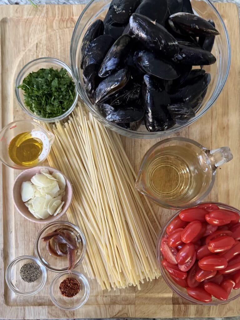 All prepped ingredients for Italian linguine with mussels on cutting board.