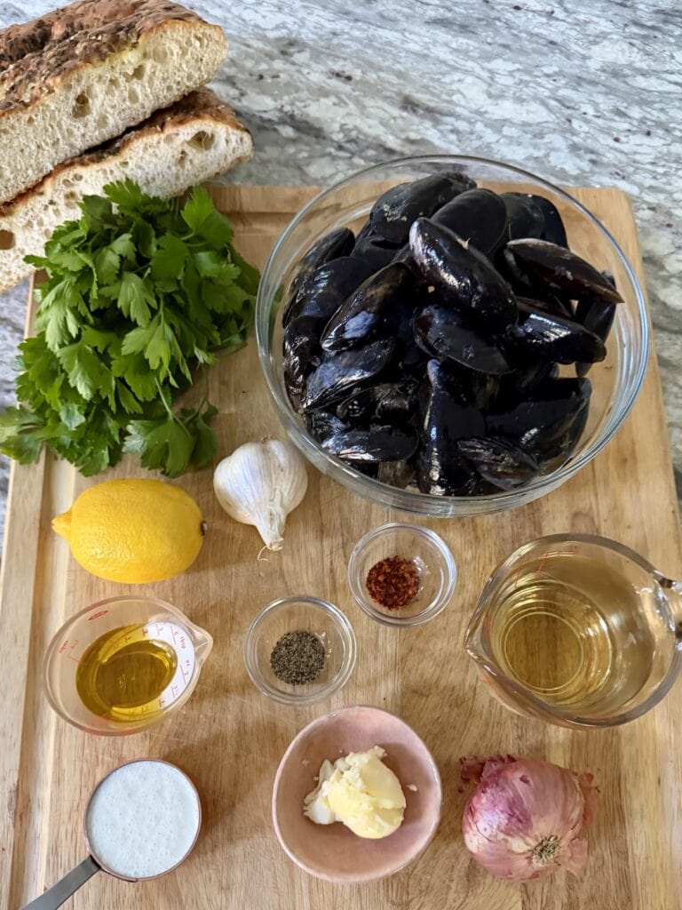 All ingredients for french style mussels with bread on cutting board.