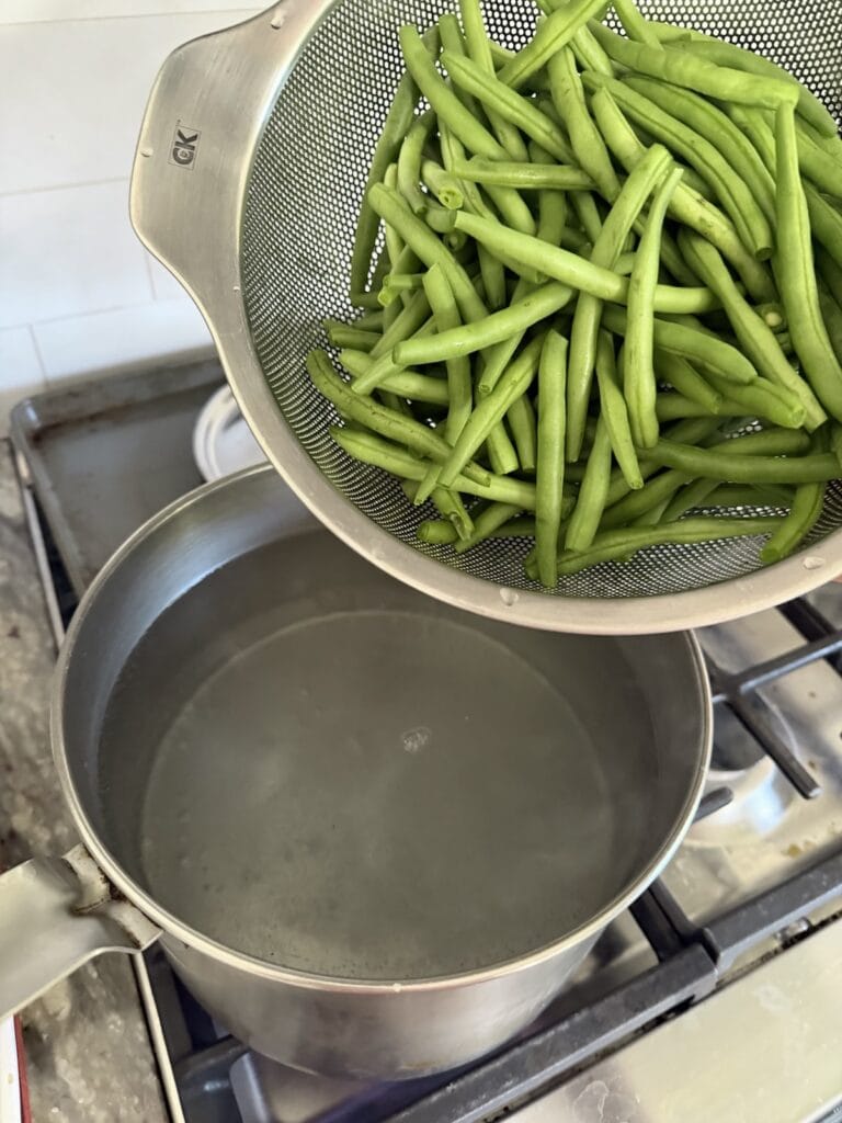 Adding raw, trimmed green beans to pot of boiling water.