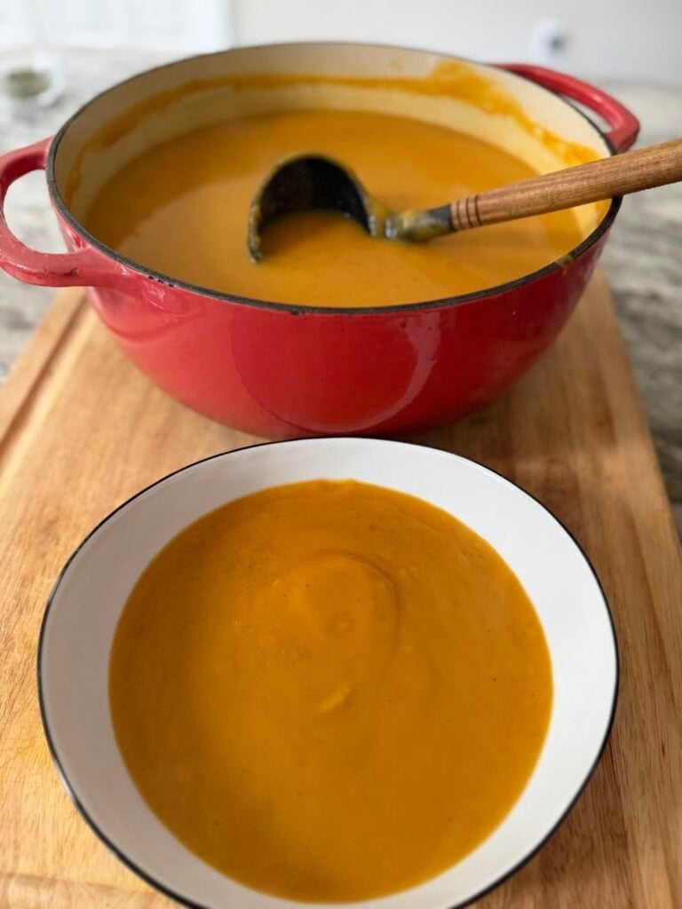 Bowl of roasted butternut soup in front of pot of it with ladle.