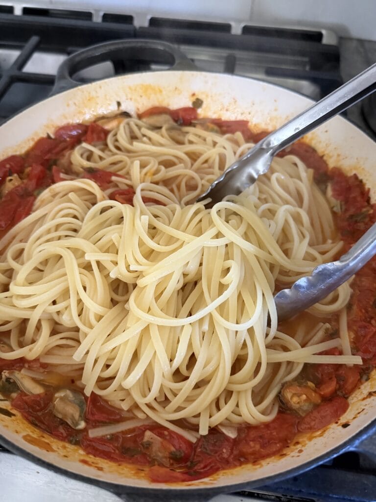 Adding cooked pasta to sauce.