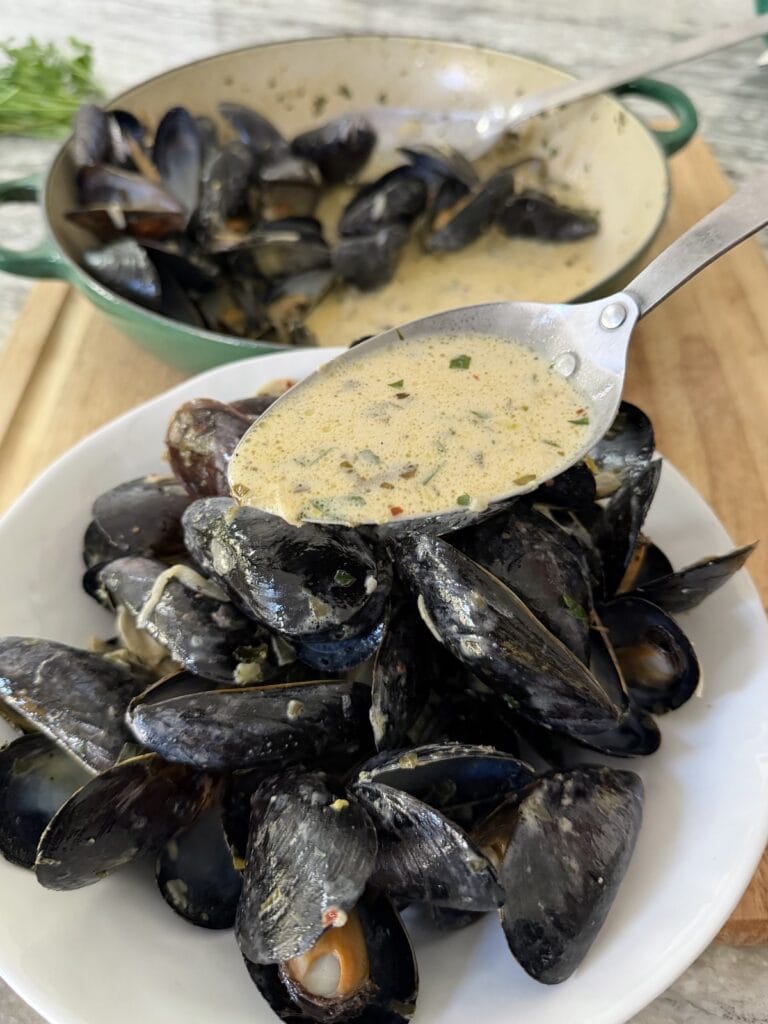 Spooning sauce over French style mussels in serving bowl.