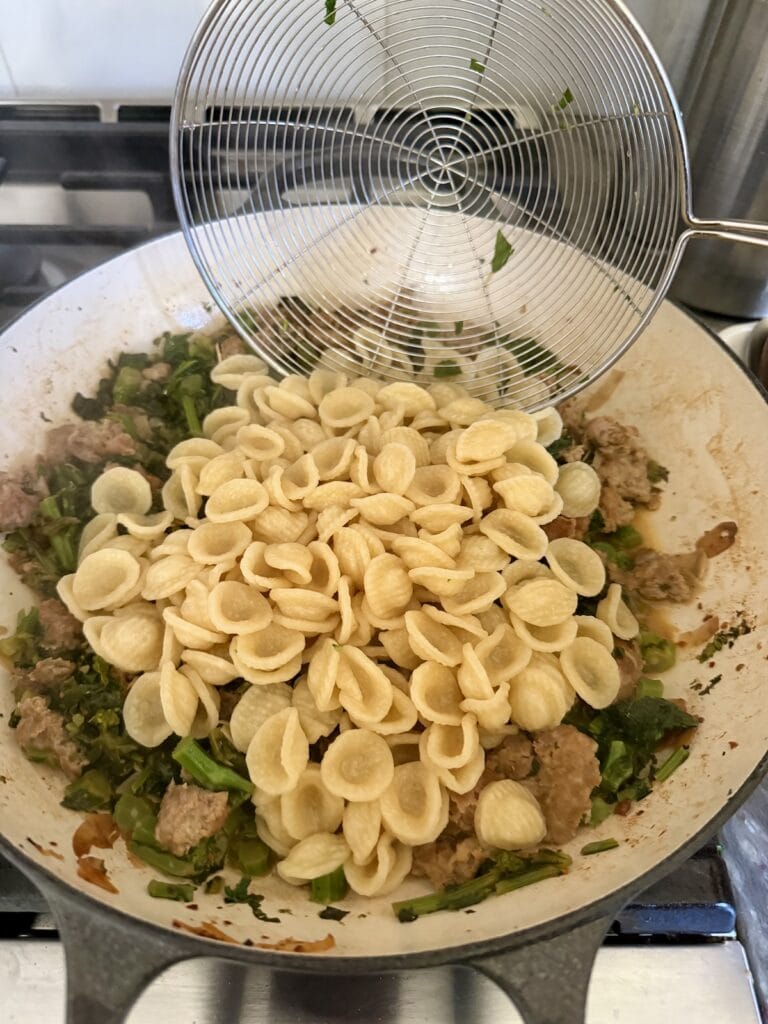 Adding cooked pasta to the sauce to finish cooking.