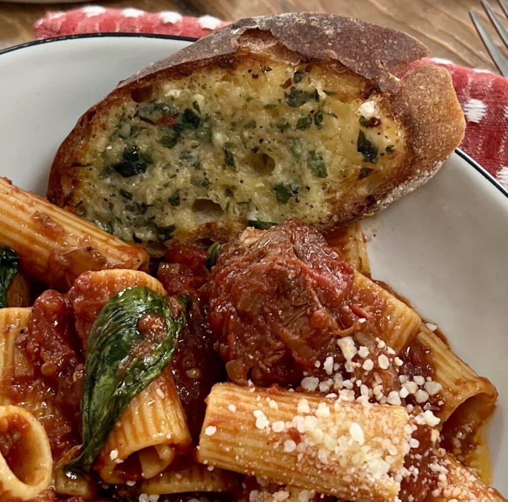 Close up of a piece of homemade garlic bread in a bowl with macaroni and gravy.