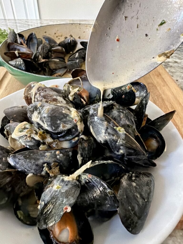 Spooning sauce over moules mariniere in serving bowl.