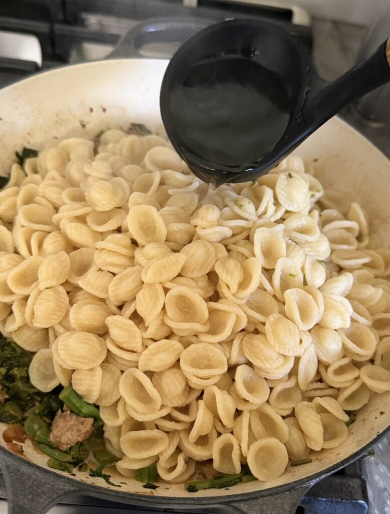 Pouring pasta water into the pasta and sauce.