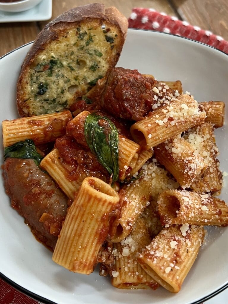 Garlic bread in bowl with pasta and Sunday sauce.