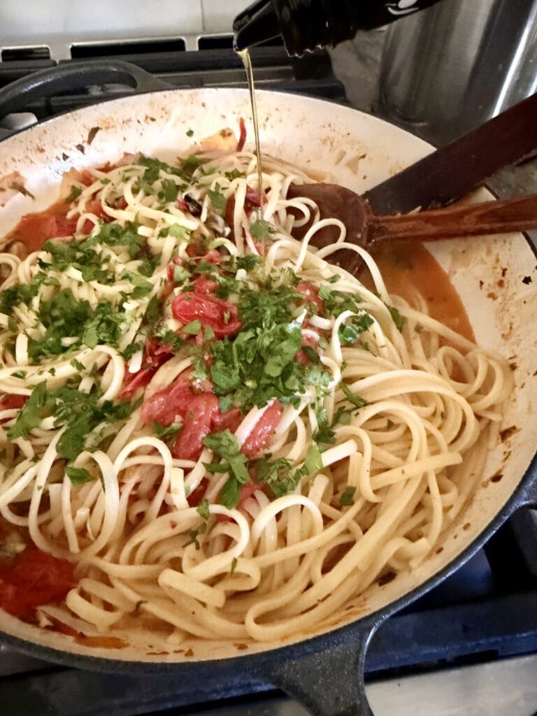 Drizzling extra virgin olive oil over pasta with chopped parsley.
