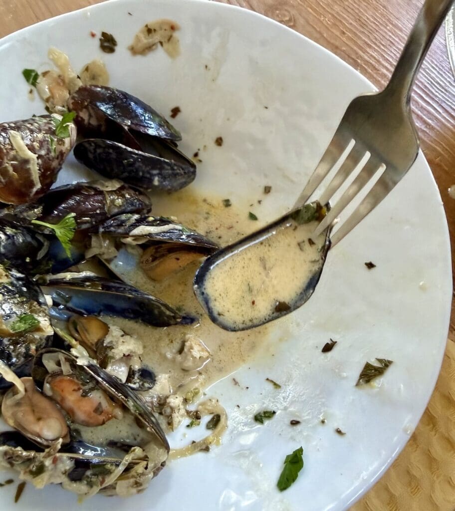 Usinf a fork and mussel shell as a spoon to pick up creamy white wine mussel sauce.