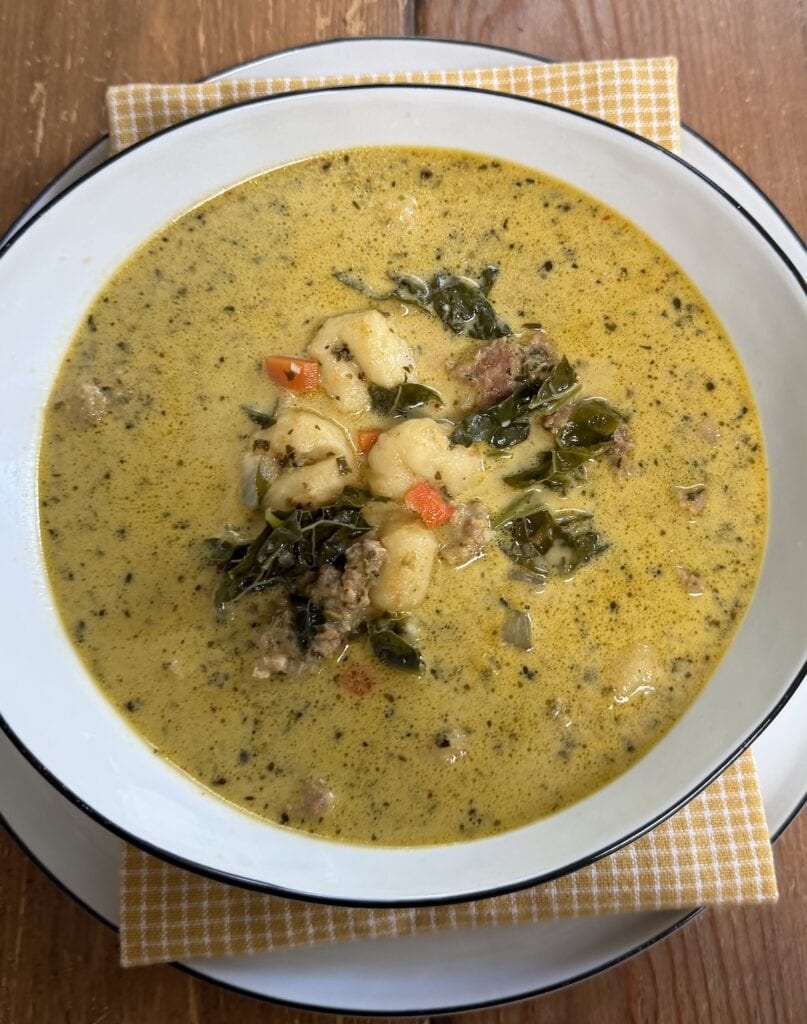 Creamy Gnocchi Sausage soup in large soup bowl over decorative towel.