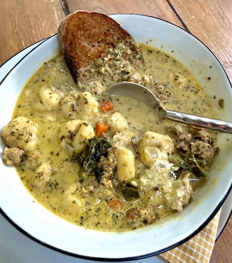 Spoon in a bowlful of creamy gnocchi sauage soup with a slice of bread.