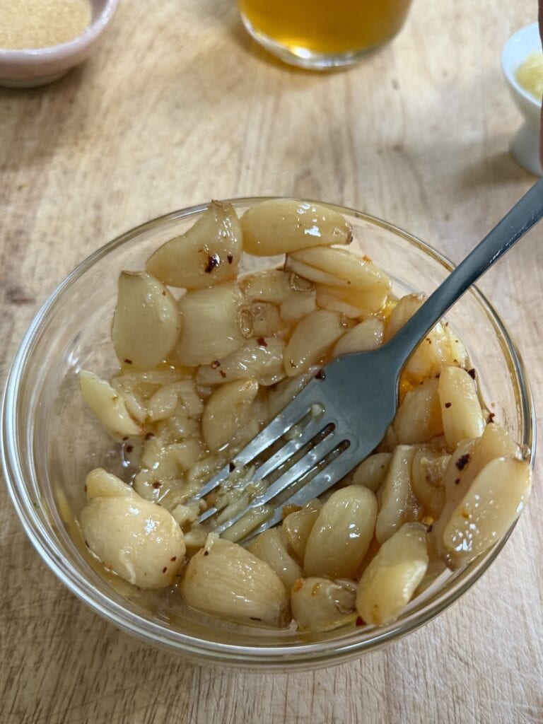 Mashing garlic confit cloves in a bowl with a fork.