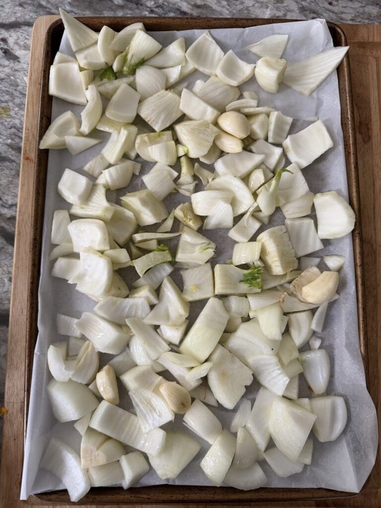 Prepped fennel, onions and garlic cloves on parchment-lined sheet pan ready for the oven.