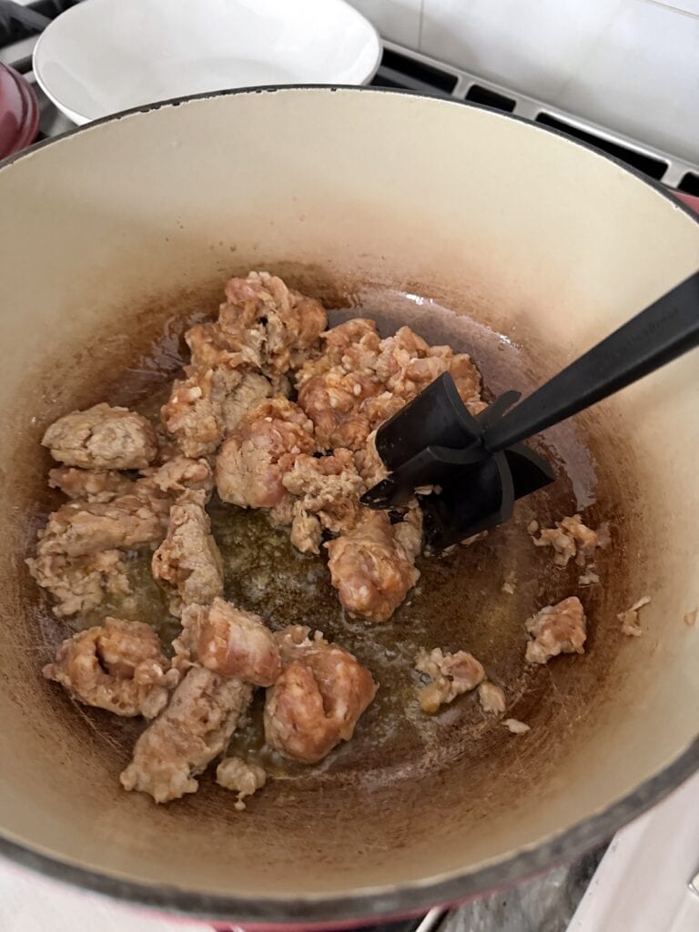 Browning sausage in Dutch oven and using meat masher to break it up into smaller pieces.