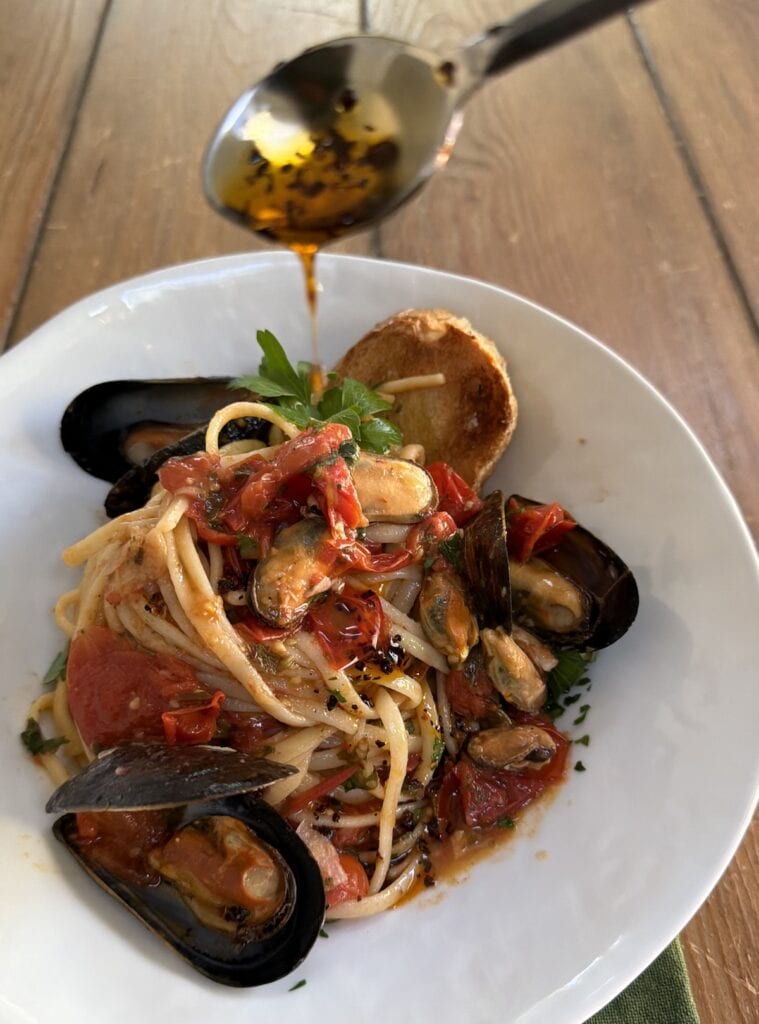Drizzling spicy pepper oil over plate of linguine and mussels.