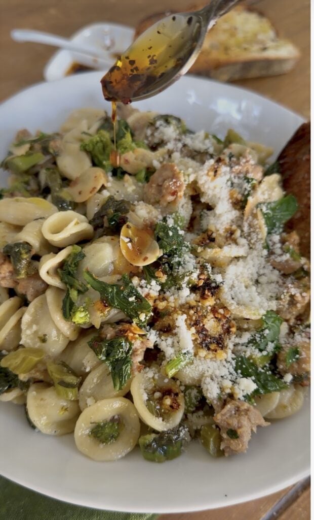 Drizzling some olio santo spicy oil over a bowlful of pasta with broccoli rabe and sausage.