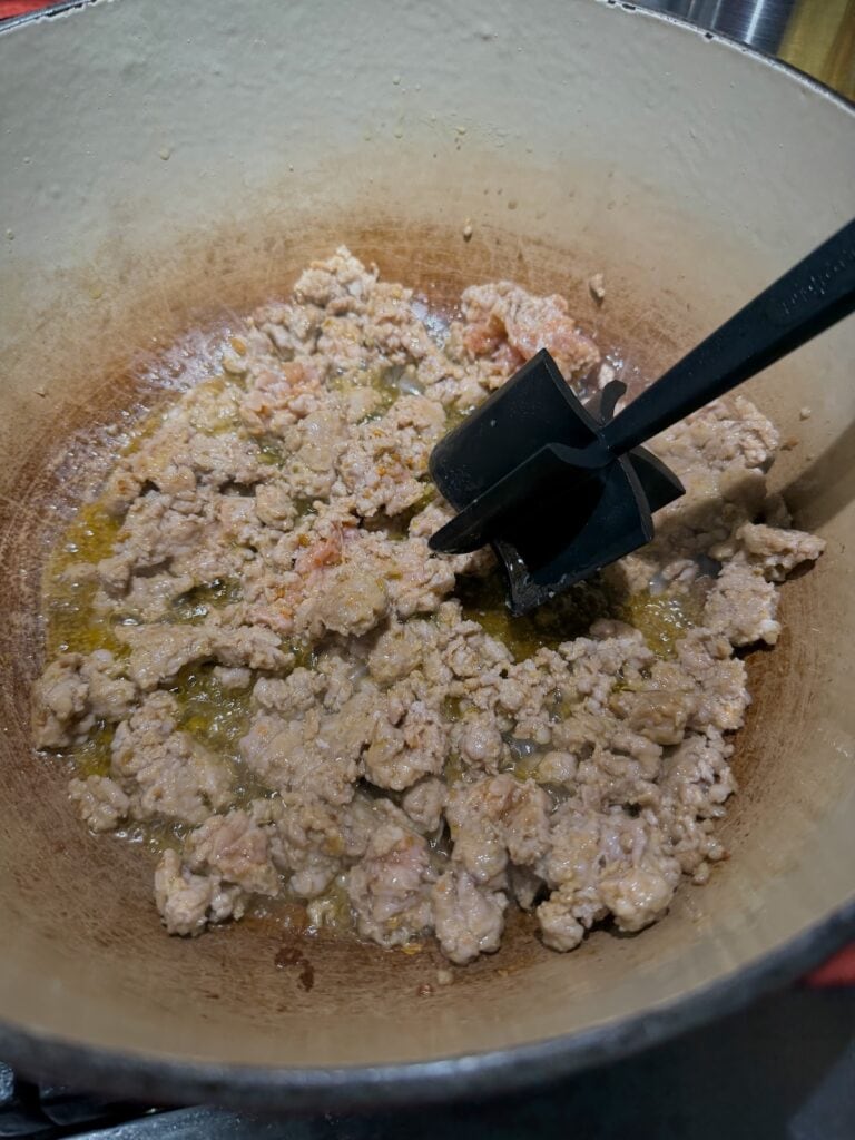 Browning meat in Dutch oven and breaking it up into smaller pieces using a meat masher.