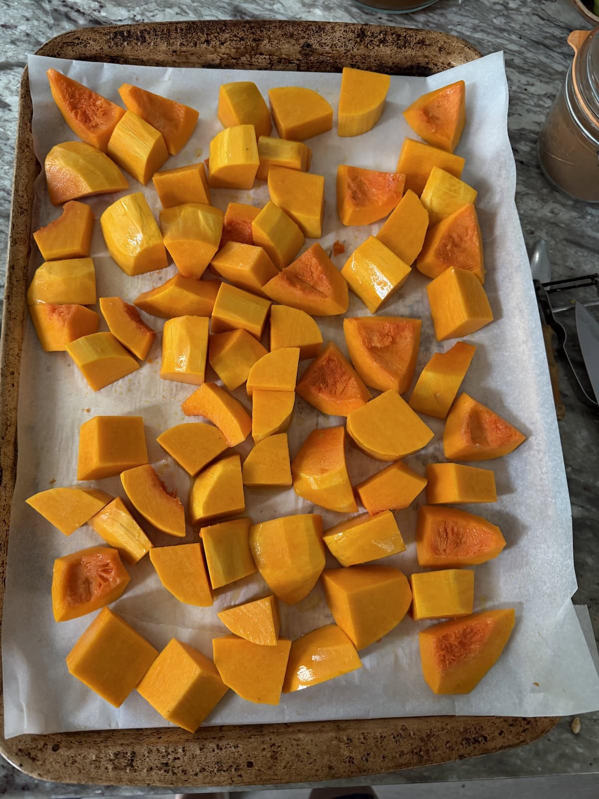 Chunks of butternut squash on parchment-lined sheet pan ready for the oven.