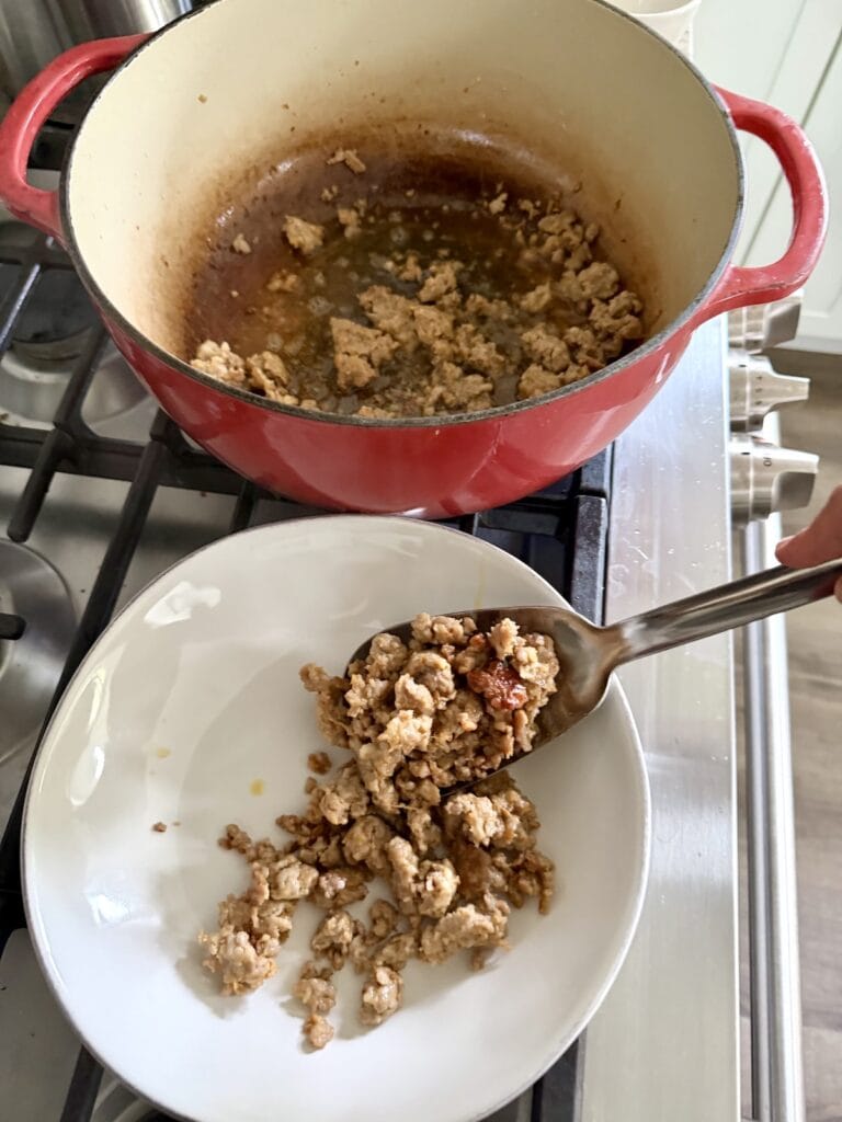 Transferring browned meat from pan to dish with slotted spoon.