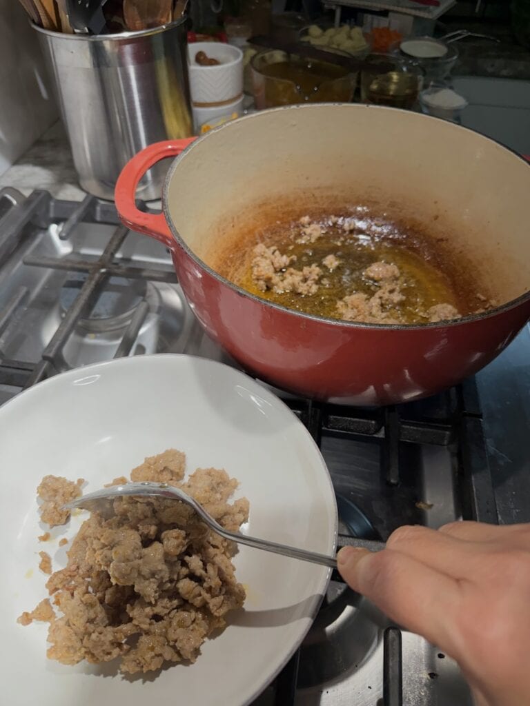 Spooning browned sausage from pot to plate.