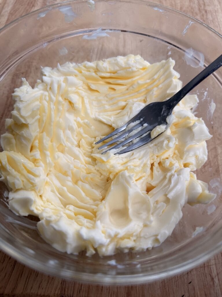 Smashing softened butter in bowl with a fork.