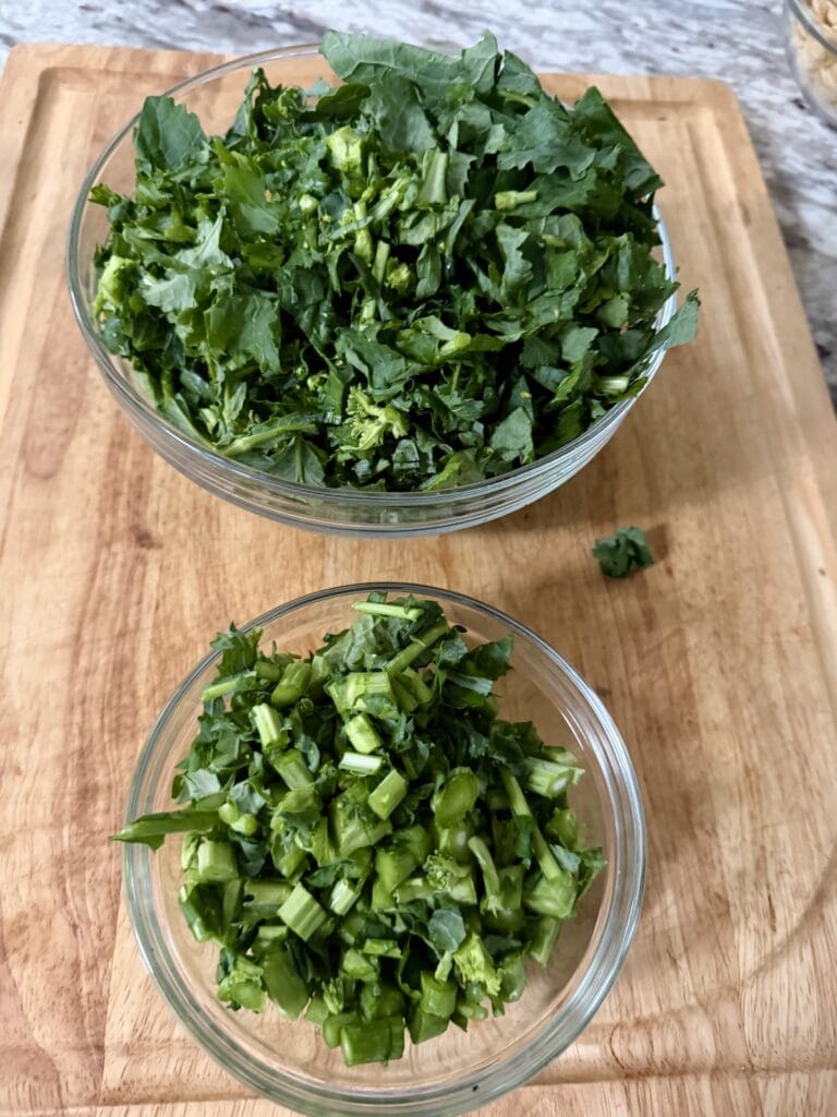 A bowl of chopped rapini stems next to a bowl of chopped rapini leaves and flowers.