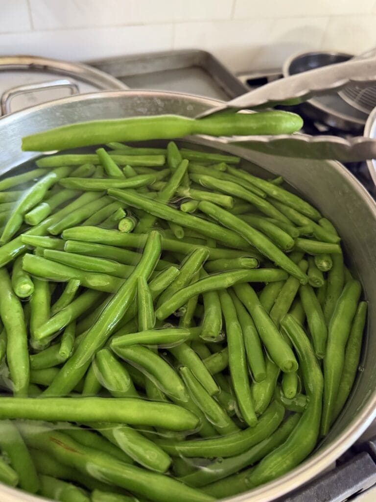 Testing one string bean's doneness with a pair of tongs.