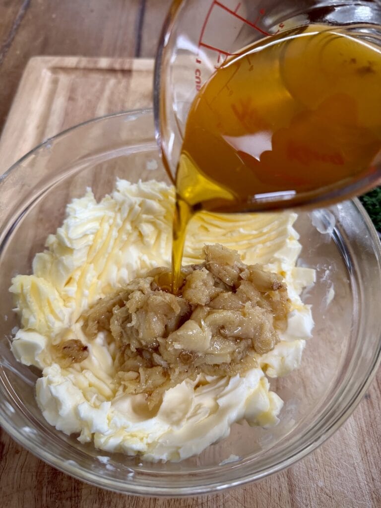 Pouring garlic oil into bowl with butter and mashed garlic confit.
