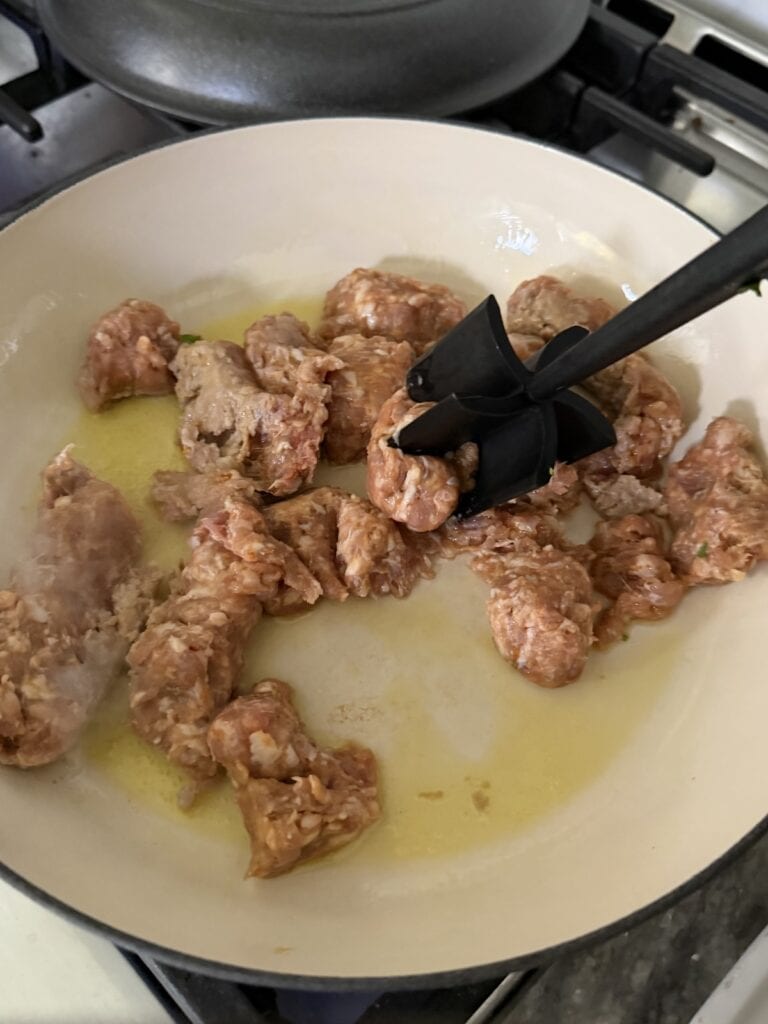 Breaking up pieces of Italian sausage i pan with a meat masher.