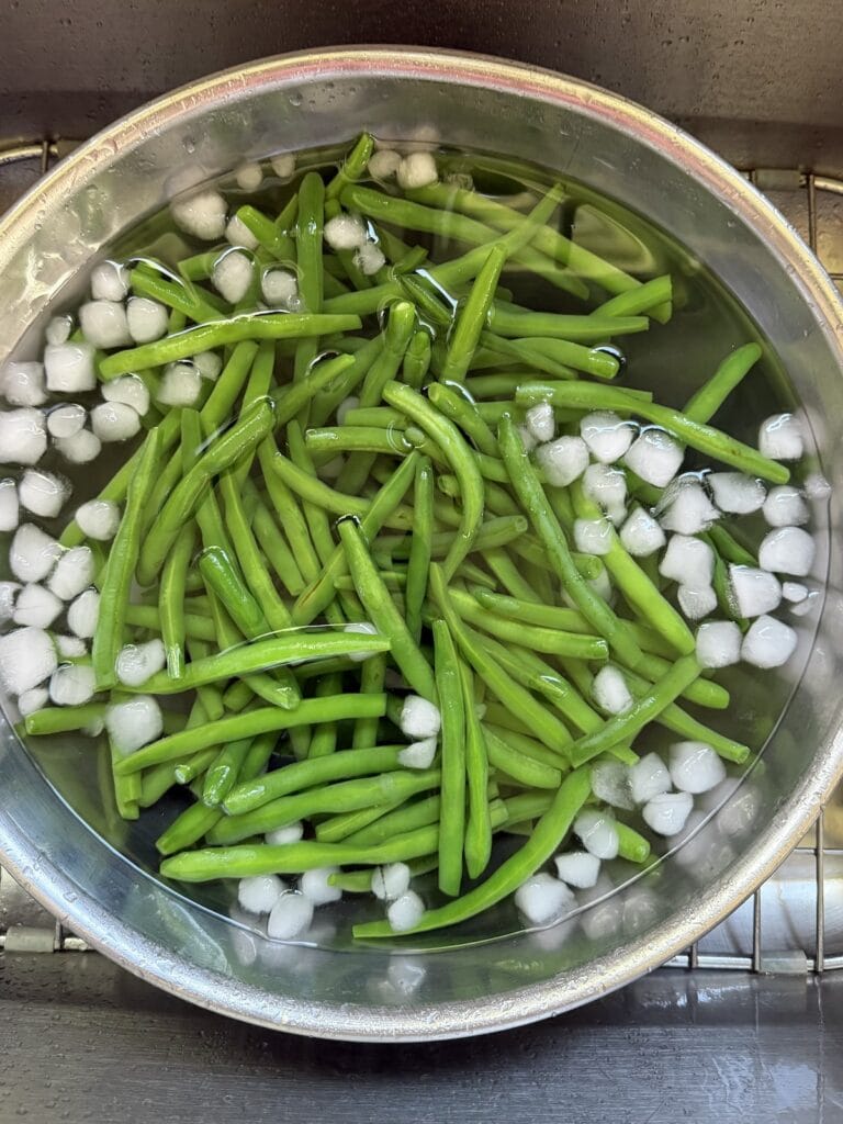 Shocking blanched green beans in bowl of ice water.