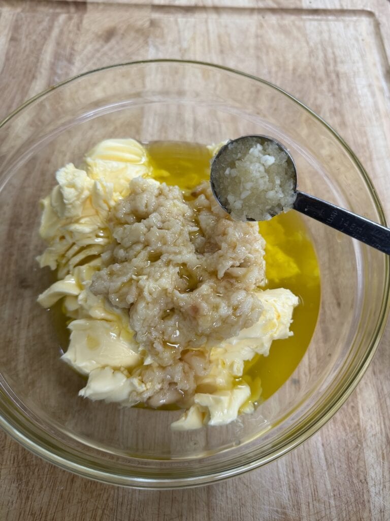 Adding minced raw garlic to bowl with other garlic butter ingredients.