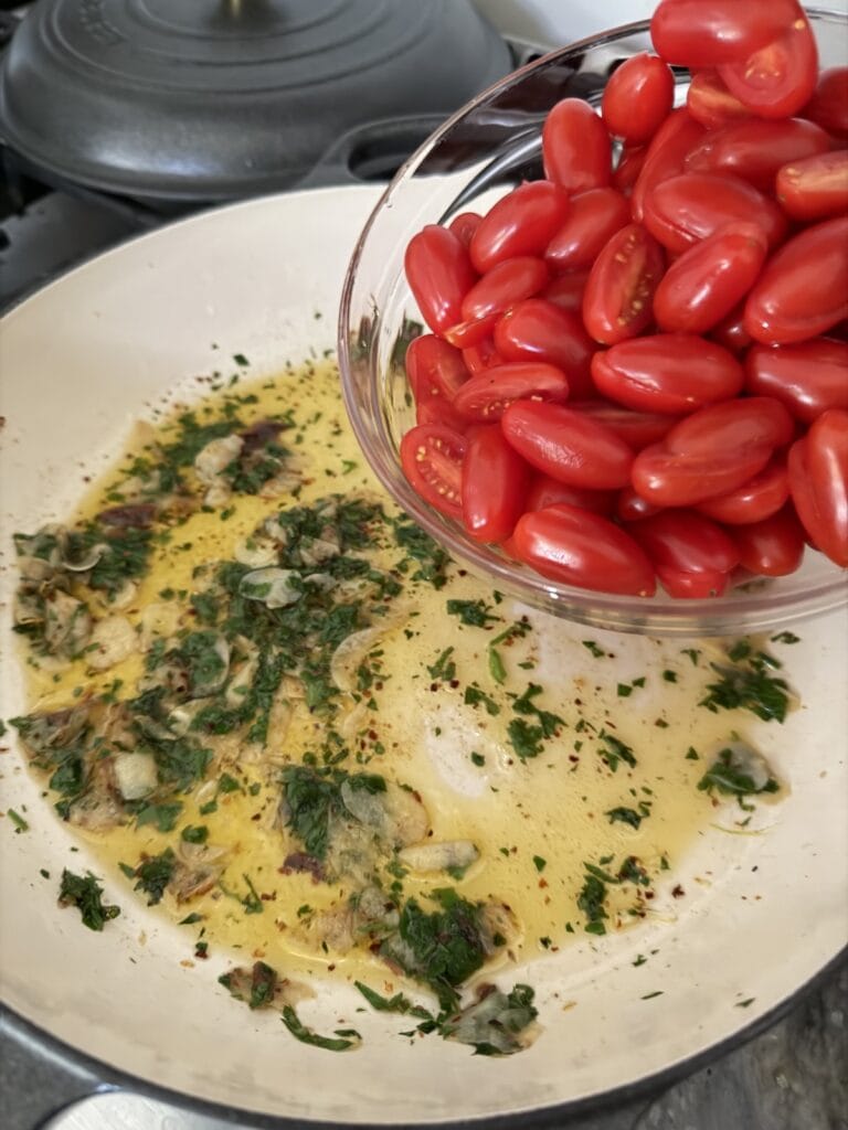Adding sliced grape tomatoes to pan.