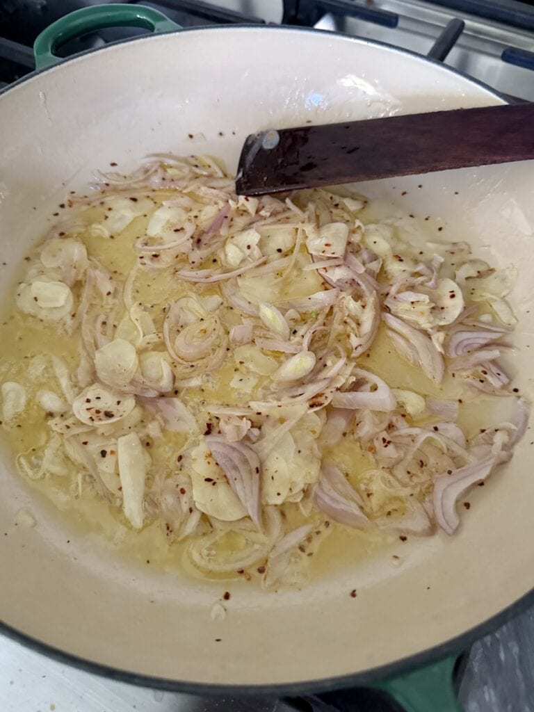 Sautéing aromatics in pan with wooden utensil for white wine mussels
