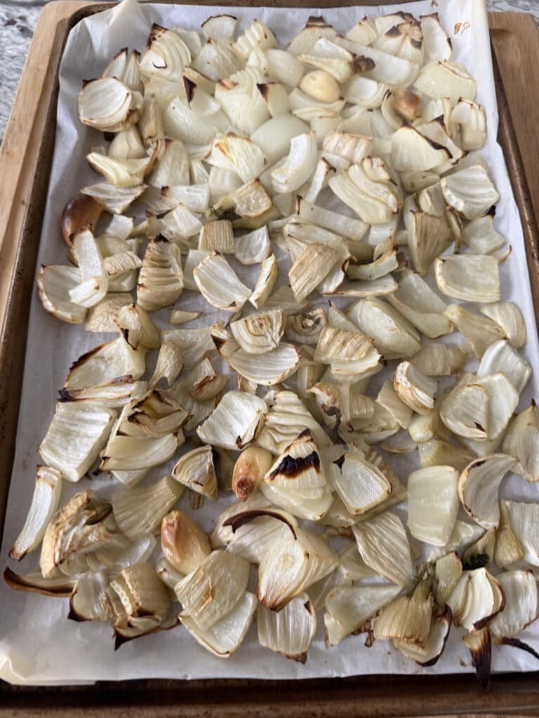 Fennel, onions and garlic on parchment-lined sheet pan after being roasted.