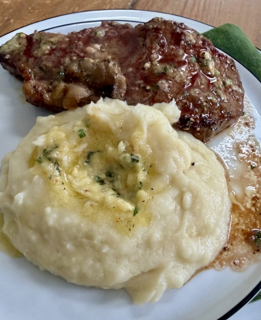 Garlic butter with herbs over mashed potatoes and steak.