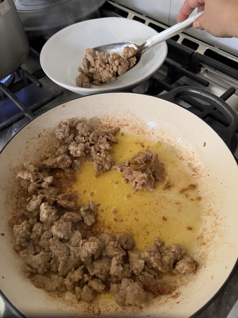 Transferring browned sausage from pan to dish.