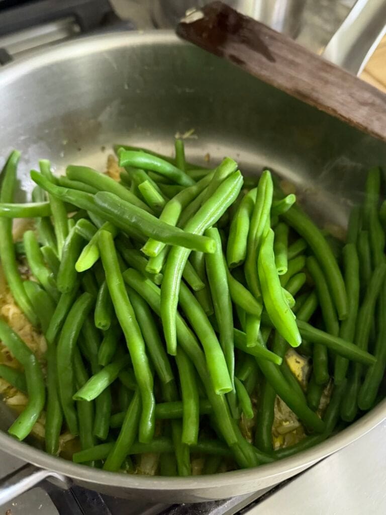 Blanched green eans added to pan to toss with sautéed garlic.