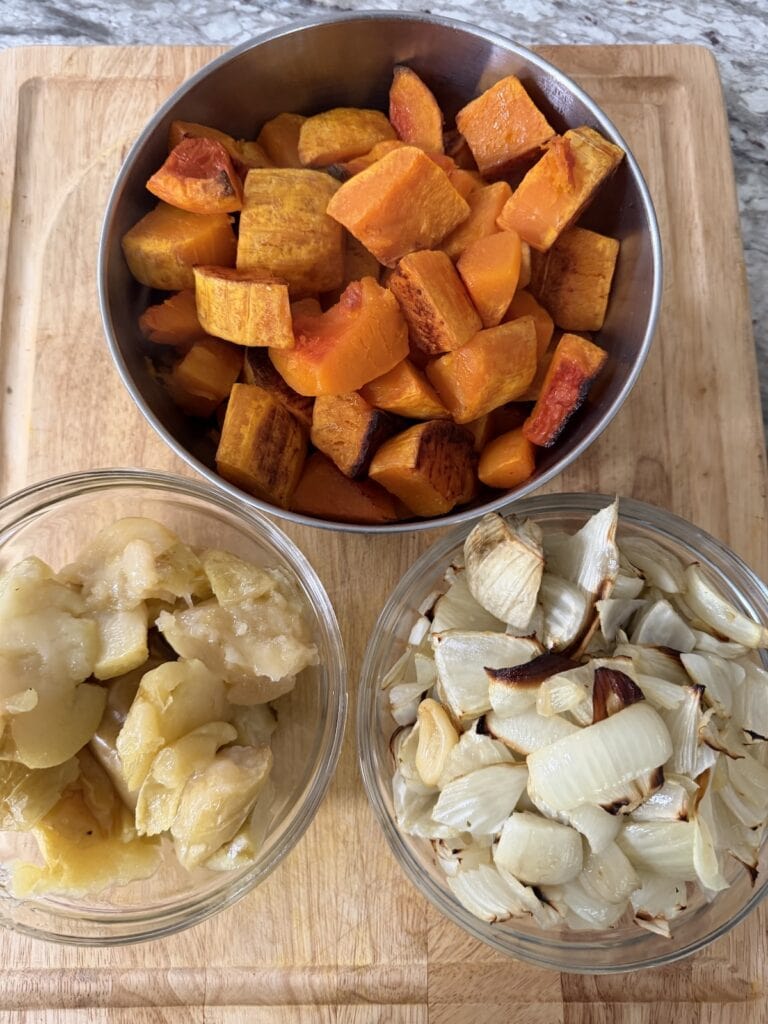 Bowls of all the roasted vegetables and apples on cutting board.