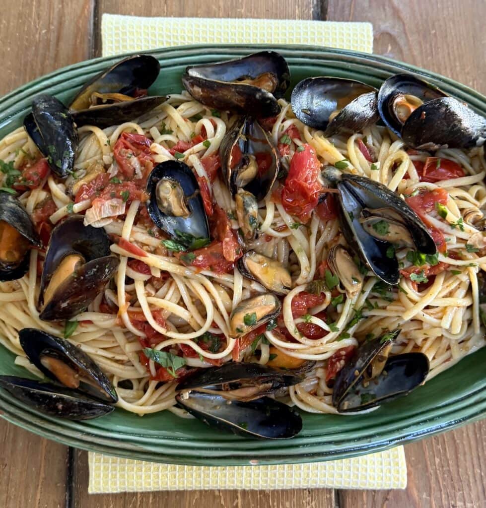 Linguine with mussels on green serving platter over yellow towel.