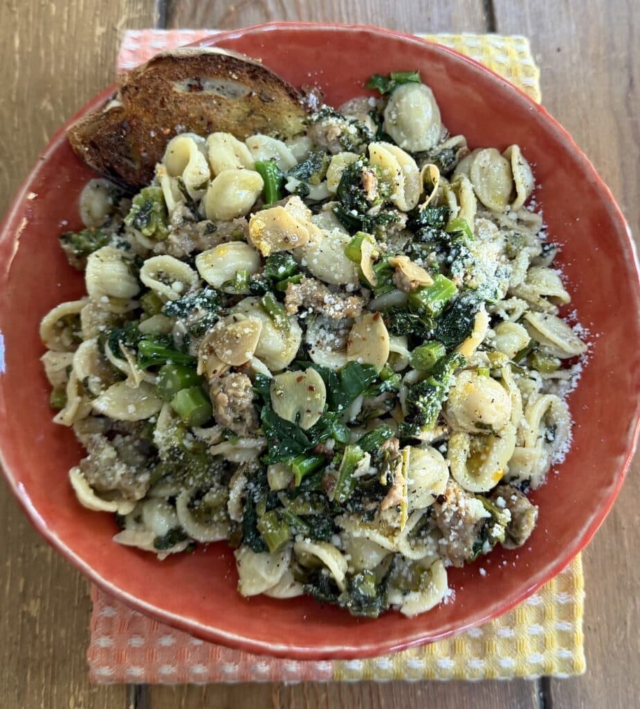 Orecchiette With Sausage and Broccoli Rabe in orange pasta bowl with piece of bread.