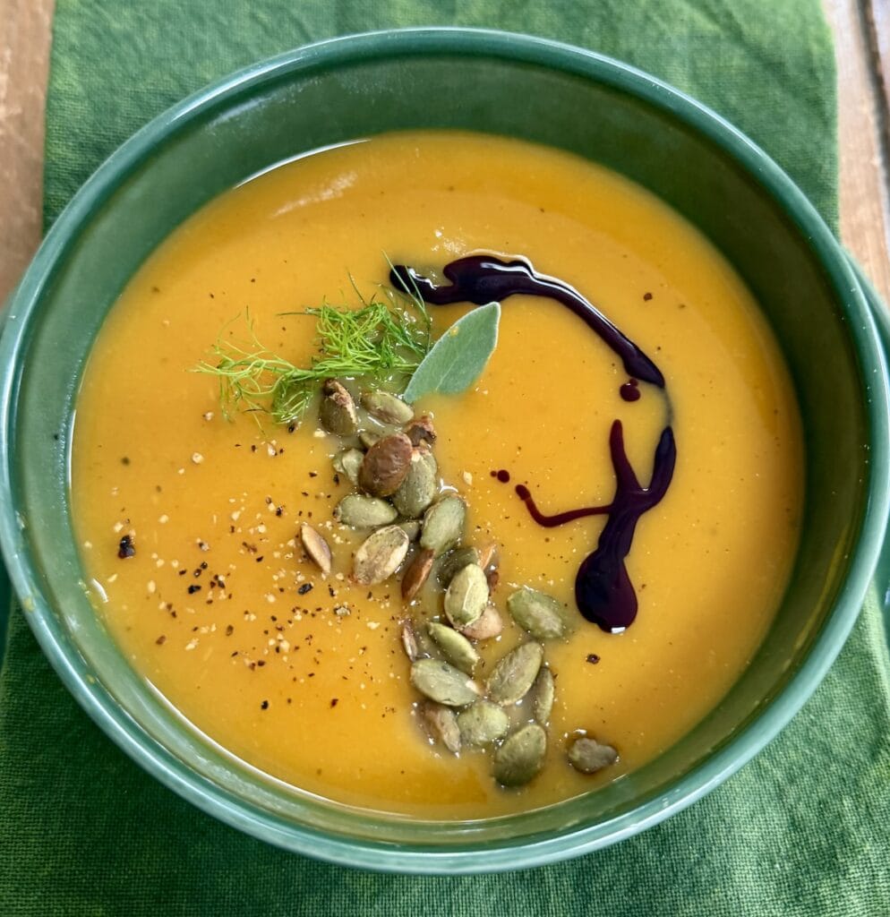 Roasted Butternut Squash Soup with Fennel, Apple and toasted pumpkin seeds in green soup bowl with garnishes.