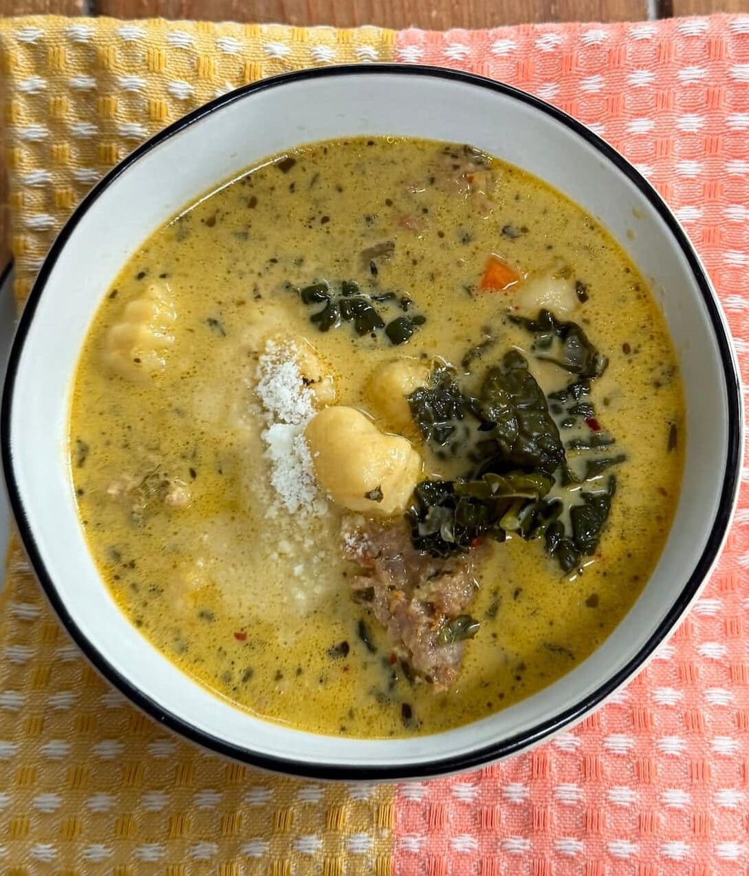 Sausage Gnocchi Soup with Kale in soup bowl with grated cheese over decorative towel.