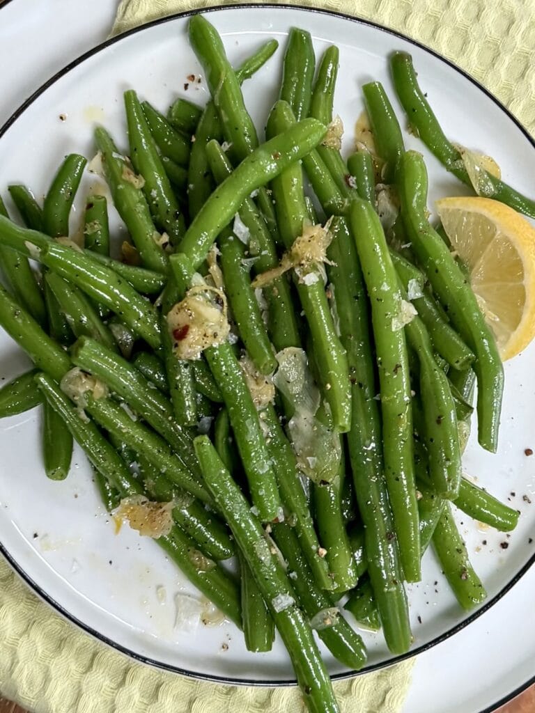 Garlicky Sauteed Green Beans with lemon wedge on white plate.